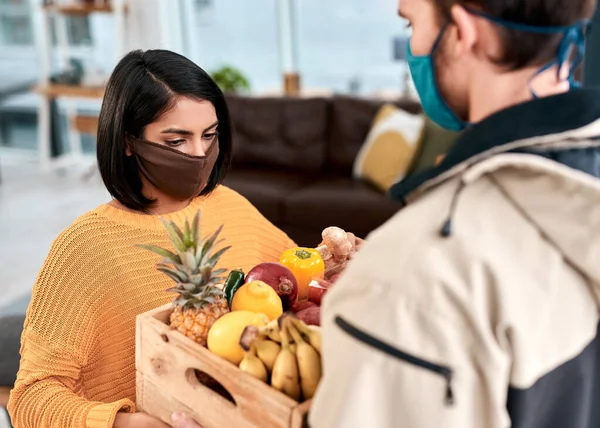 The home delivery business is booming during lockdown. a masked young woman receiving a delivery of fresh fruit and vegetables at home