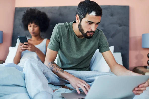 Ill find us something to watch. a man using his laptop while his girlfriend sits on her phone in the background