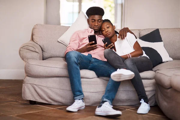 Lets just find something to watch. a couple using their cellphones while relaxing on the sofa at home