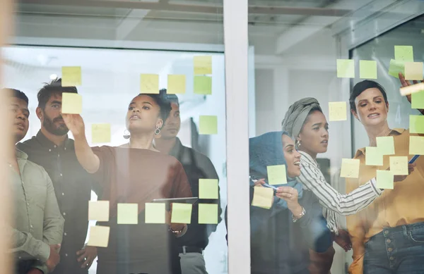 They have so many amazing ideas going around. a group of businesspeople brainstorming with notes on a glass wall in an office