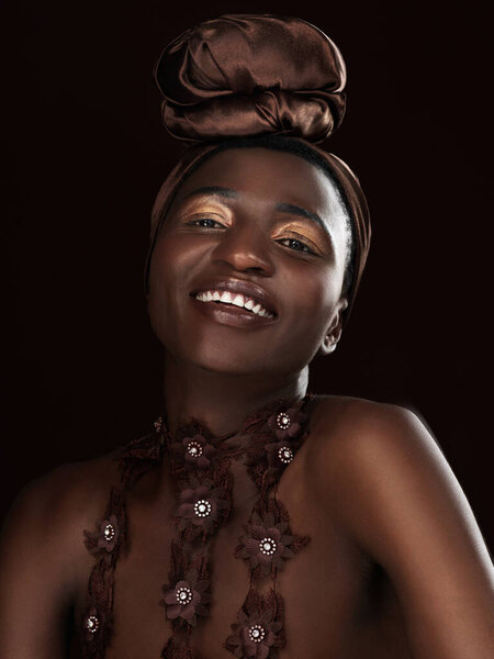 Showing her beauty through her smile. Studio portrait of an attractive young woman posing in traditional African attire against a black background