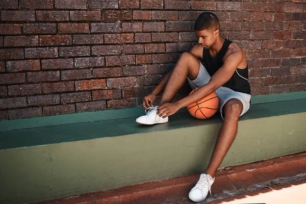 The harder you work, the harder it is to lose. a sporty young man tying his laces while playing basketball outdoors