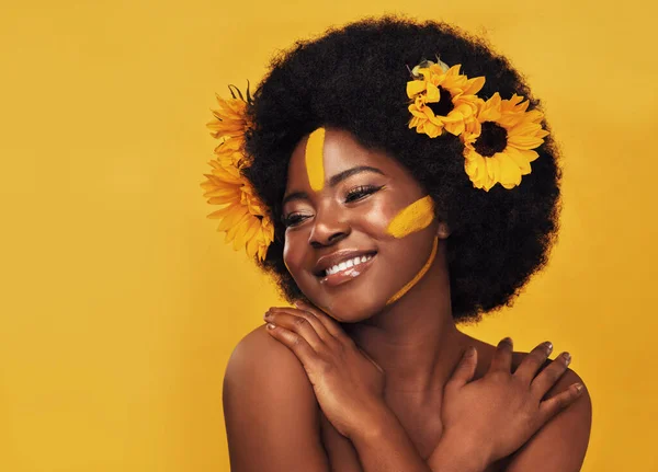 I feel pretty in my yellow wreath. Studio shot of a beautiful young woman smiling while posing with sunflowers in her hair against a mustard background