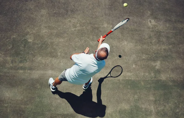 What a shot. High angle shot of a focused middle aged man playing tennis outside on a tennis court during the day