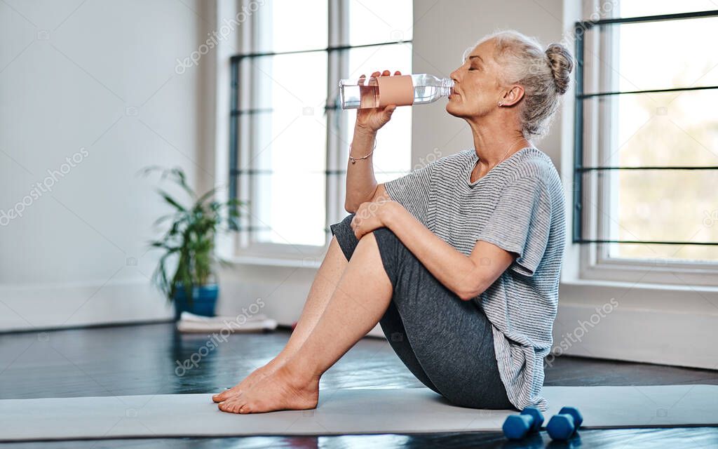 Bottoms up. a mature woman practicing yoga while having a drink of water inside of a studio during the day