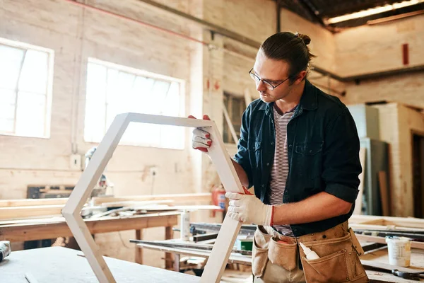 Just making sure everything fits perfectly. a handsome young carpenter working on a wooden frame inside a workshop