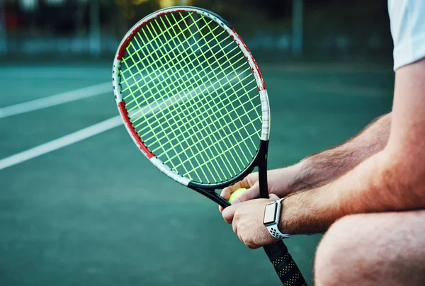 Today I will advance to a new level. Closeup shot of an unrecognisable man holding a tennis racket and ball on a tennis court