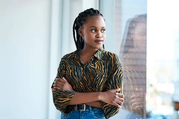 Every business started with just an idea. an attractive young businesswoman looking contemplative while standing with her arms folded in her office alone