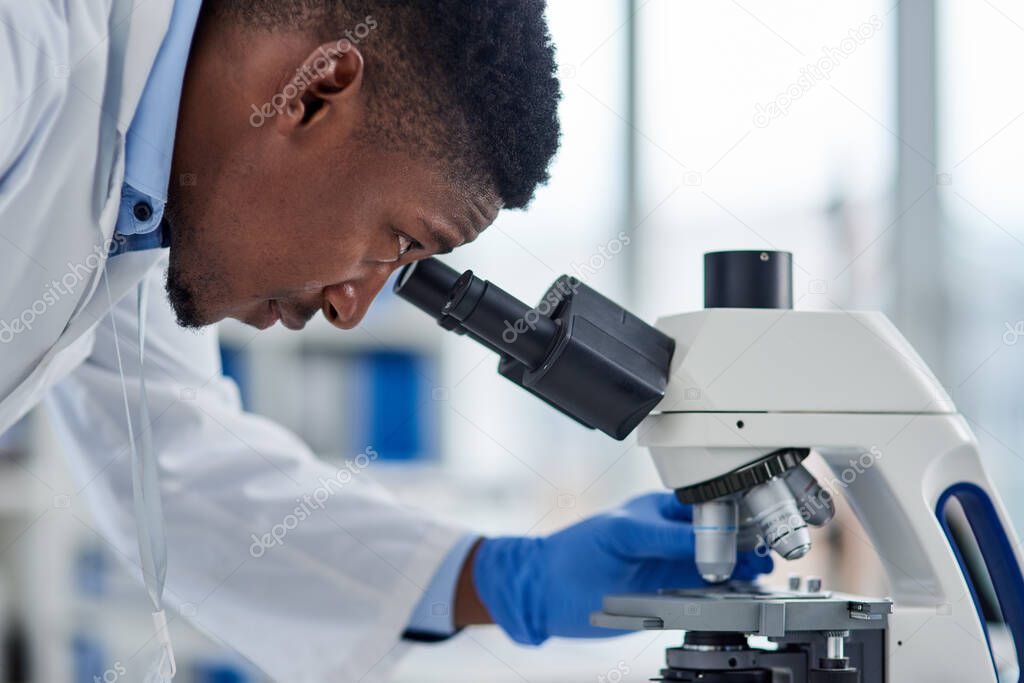 Lets have a look. a focused young male scientist looking at test samples through a microscope inside of a laboratory during the day