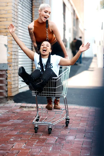 Friends make trolleys fun. Full length shot of two cheerful young girlfriends having fun with a shopping cart outdoors during the day