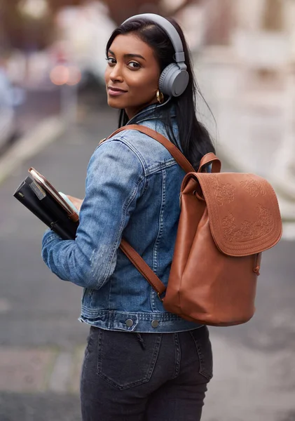 You have to start on your future today. a young woman walking through the city wearing headphones while carrying her books
