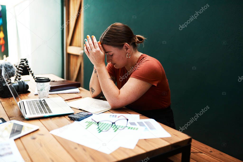 This is so overwhelming. an attractive young businesswoman sitting alone at her desk and suffering from a headache