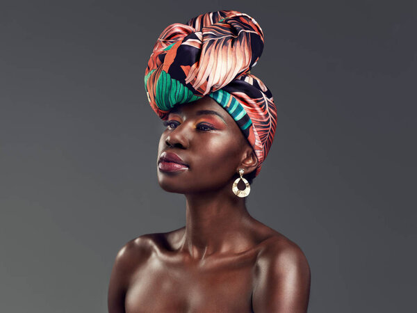 Haute couture meets heritage. Studio shot of a beautiful young woman wearing a traditional African head wrap against a grey background