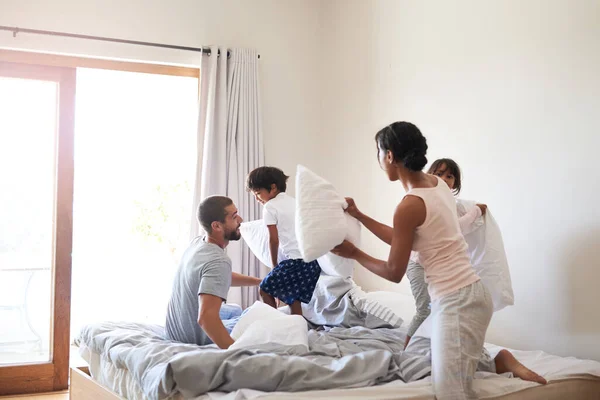 Take cover. a beautiful young family of four pillow fighting in bed at home