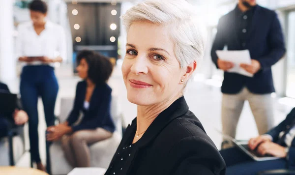 Im smiling because I know that we handle the pressure. Cropped portrait of an attractive mature businesswoman sitting and smiling while her colleagues work behind her in the office