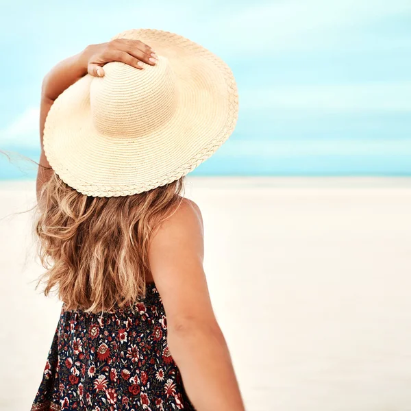 Make sure you get your sunhat out. Rearview shot of a young woman spending the day at the beach