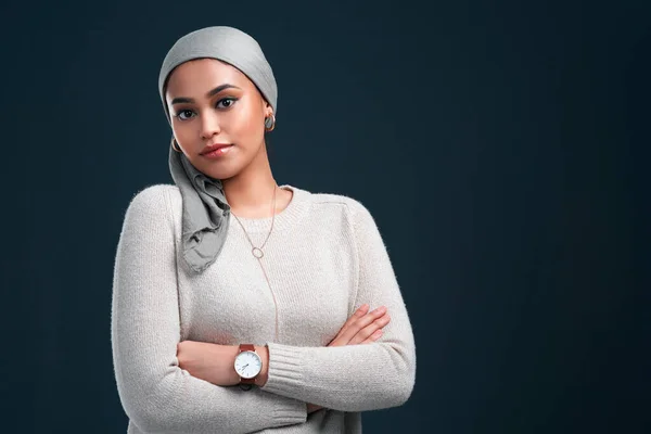 I am proud to be muslim. an attractive young woman wearing a headscarf and standing with her arms folded against a black background