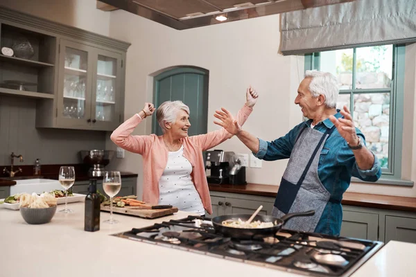 Good food puts everyone in a good mood. a senior couple dancing while cooking in the kitchen at home