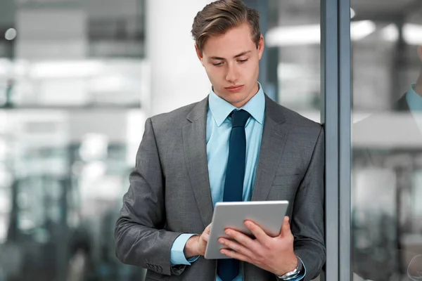 Checking my to-do list. a handsome young businessman standing alone in his office and using a tablet