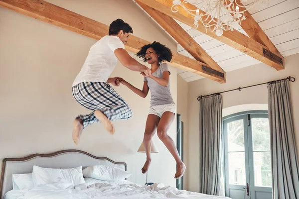 Were taking a leap of faith together. Full length sho of a playful young couple jumping on bed together at home