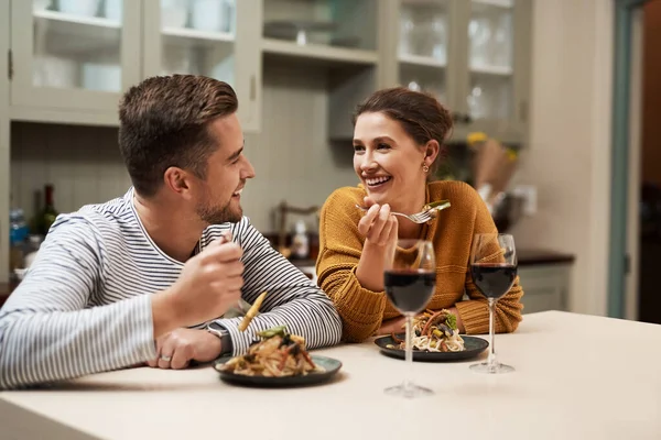 Who doesnt love a home cooked meal. an affectionate young couple smiling at each other while enjoying dinner in their kitchen at home