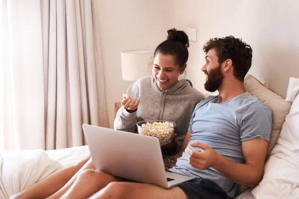 Who said dates have to be fancy. a happy young couple using a laptop and eating popcorn while relaxing on the bed at home