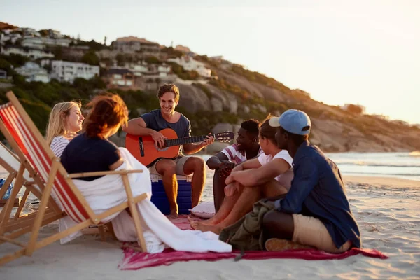 Having a beautiful bonding experience at the beach. a man playing the guitar while sitting on the beach with his friends