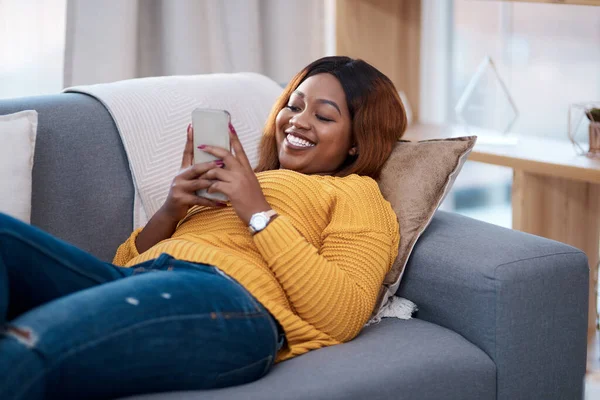 Home is my happy place. an attractive young woman using her cellphone while relaxing on the sofa at home