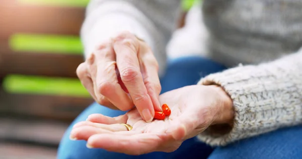 This will make me feel better. an unrecognizable elderly woman about to take medication outside in a park during the day