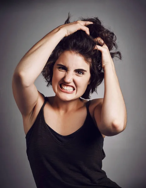 Cant contain the rage. Studio portrait of an attractive young woman pulling her hair with rage while standing against a grey background