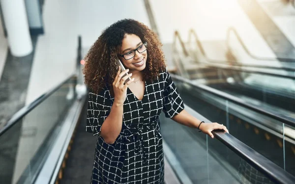 She closes good deals with just one phone call. High angle shot of an attractive young businesswoman taking a phonecall while going up an escalator in a modern office