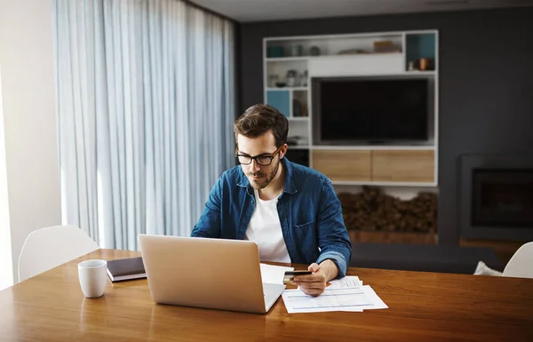 Time to have a look at whats on special online. a handsome young businessman sitting down and using his laptop to do some online shopping while working from home