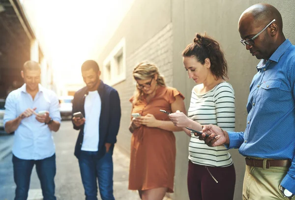 Diverse group of adult people connecting and social networking outside. Businesspeople texting, browsing and sharing information on phones online while out of the office on a break from work