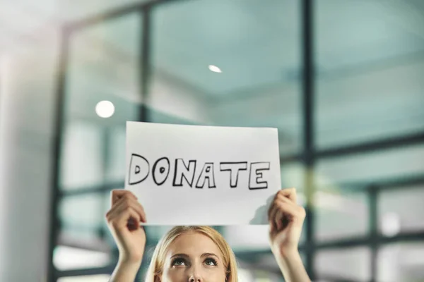 A woman asking for a donation, charity and help while holding a sign in need of support in a corporate office. Volunteer asking for assistance and crowdfunding from the community and businesses.