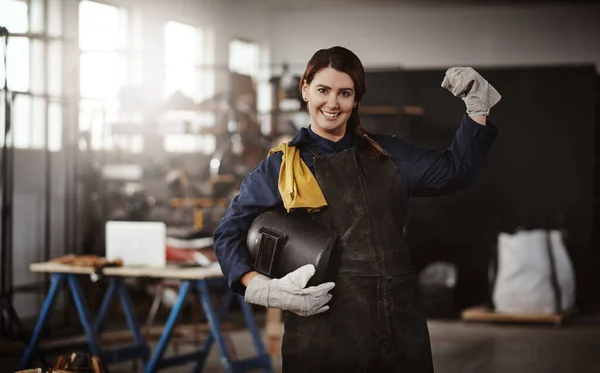 I can do anything a man can do. Cropped portrait of an attractive young creative female artisan flexing in her workshop with her helmet tucked under her arm