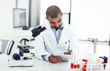 Scientist writing DNA results from microscope test on a tablet.Professional male doctor in a lab working with research tubes.Man in a modern laboratory doing medical science data analysis
