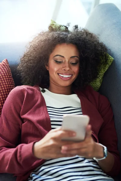 Connect with good company. a young woman using a mobile phone while relaxing on the sofa at home