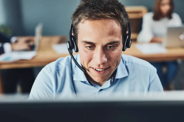 Closeup of a young male call center agent consulting and giving support while working in a busy office. Face of a man and helpdesk worker or phone operator having a conversation.