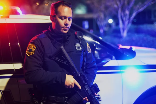 This is not an easy job. a handsome young policeman standing with his assault rifle while out on patrol