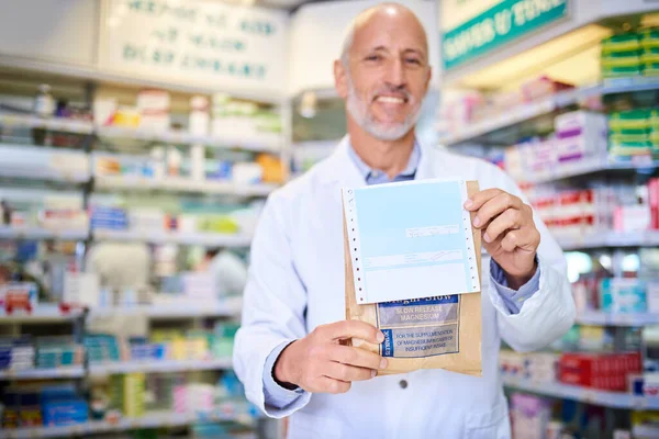Your prescription is ready for collection. Portrait of a mature pharmacist holding a paper bag with medication in a chemist