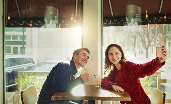 First rule of a first date Take a selfie. a young man and woman taking selfies on a date at a coffee shop