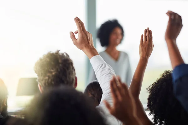 Shell get to every question eventually. Rearview shot of a group of businesspeople with their hands raised during a seminar