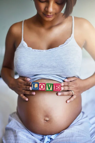 So much love for my little one. a young pregnant woman with wooden blocks on her belly that spell the word love