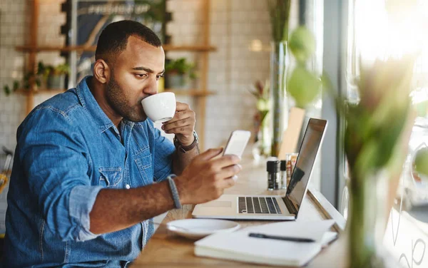 Multitasking as its finest. a handsome young businessman sitting in a cafe and drinking a cup of coffee while using technology