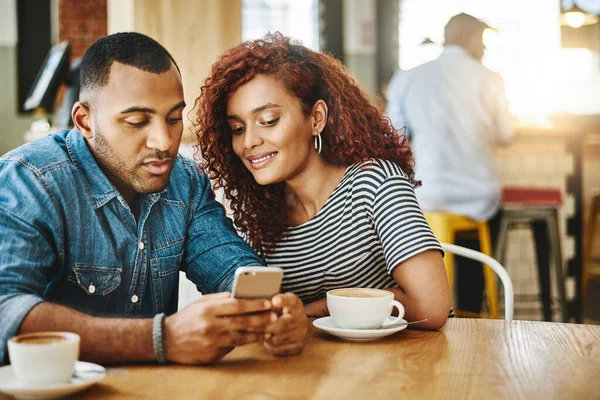 Check this out. an affectionate young couple looking at a cellphone while sitting in a coffee shop