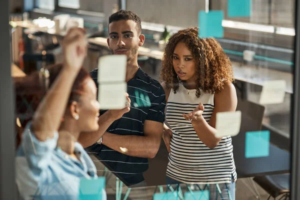 Their big plans are still a work in progress. a group of young designers brainstorming with notes on a glass wall in an office