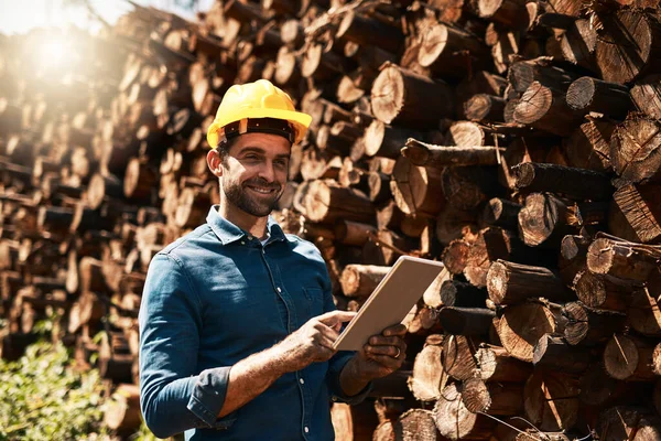 Hes the man for all your lumber needs. a lumberjack using his tablet while standing in front of a pile of wood