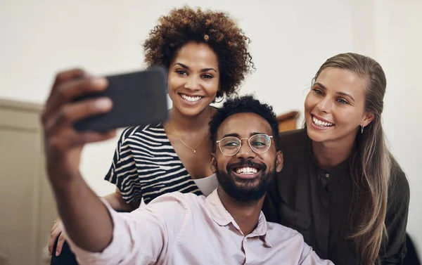 Group of office friends taking a happy selfie using a phone in business place. Cheerful, excited and joyful colleagues, work team and coworkers taking fun photos together