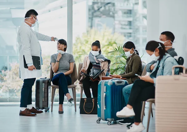 Covid doctor taking temperature of travel passengers in covid masks during tourism in an airport with an infrared thermometer. Medical professional following safe protocol in an epidemic or outbreak.