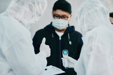 Negative covid test and thumbs up for young man from healthcare worker after testing for virus. Medical professionals in hazmat suits taking temperature tests during disease outbreak or pandemic.